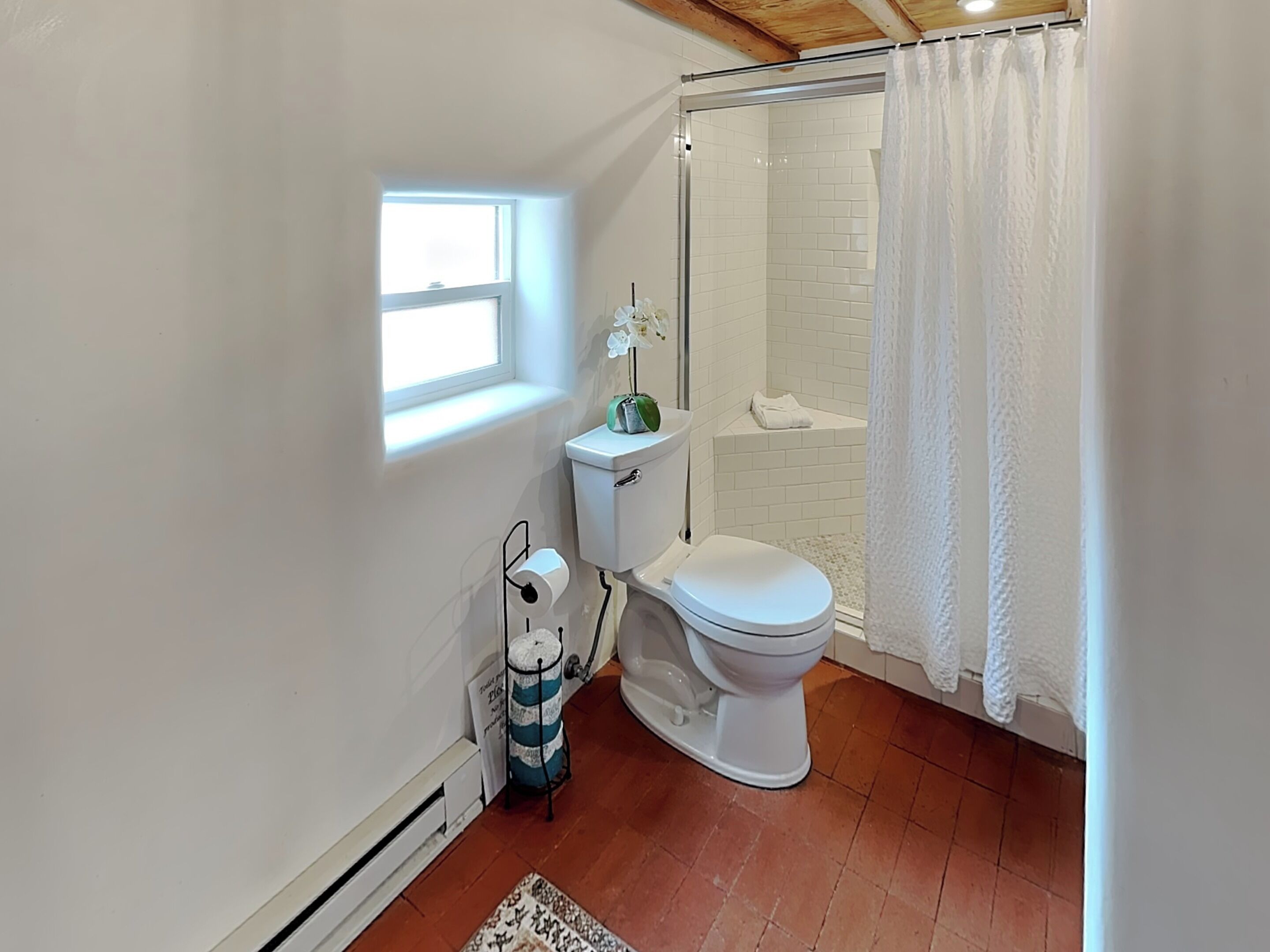 A bathroom with a toilet, shower, and a window.