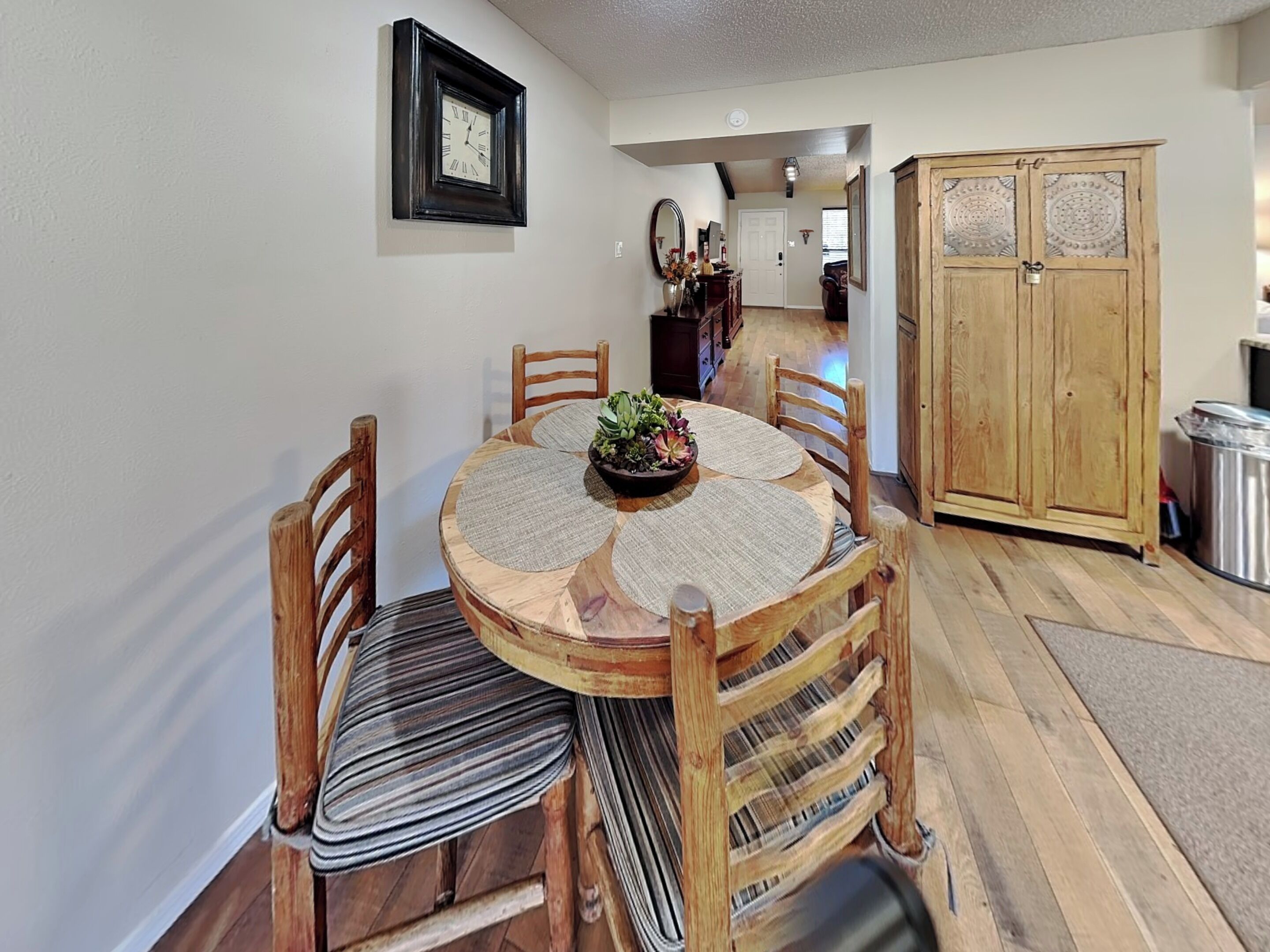 A dining area with a round wooden table, four chairs, and a clock on the wall.