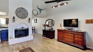 Un salon spacieux doté d’une cheminée, d’un plancher en bois, d’un grand téléviseur et d’un meuble en bois.