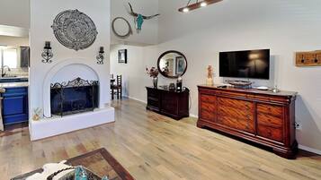 A spacious living room with a fireplace, wooden flooring, a large TV, and a wooden cabinet.
