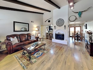 A spacious living room with a fireplace, a dining area, and a kitchen in the background. - Billy The Kid (Ruidoso)
