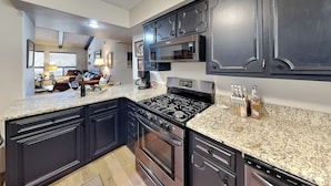 Une cuisine moderne dotée de meubles sombres, de plans de travail en granit, d’une cuisinière à gaz et d’un four à micro-ondes encastré.