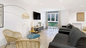 Ein modernes Wohnzimmer mit Sofa, Sesseln, einem Fernseher und einer Essecke mit Tisch und Stühlen.