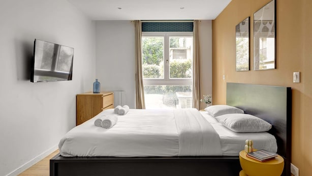 Ein modernes Schlafzimmer mit einem Bett, einem an der Wand montierten Fernseher und einem Fenster mit Vorhängen.