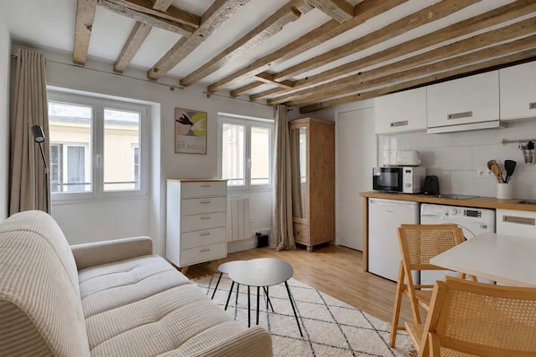 A modern kitchen with white cabinets, a coffee machine, and a dining area with a white table and chairs. - Cocon parisien en plein paris (Paris)