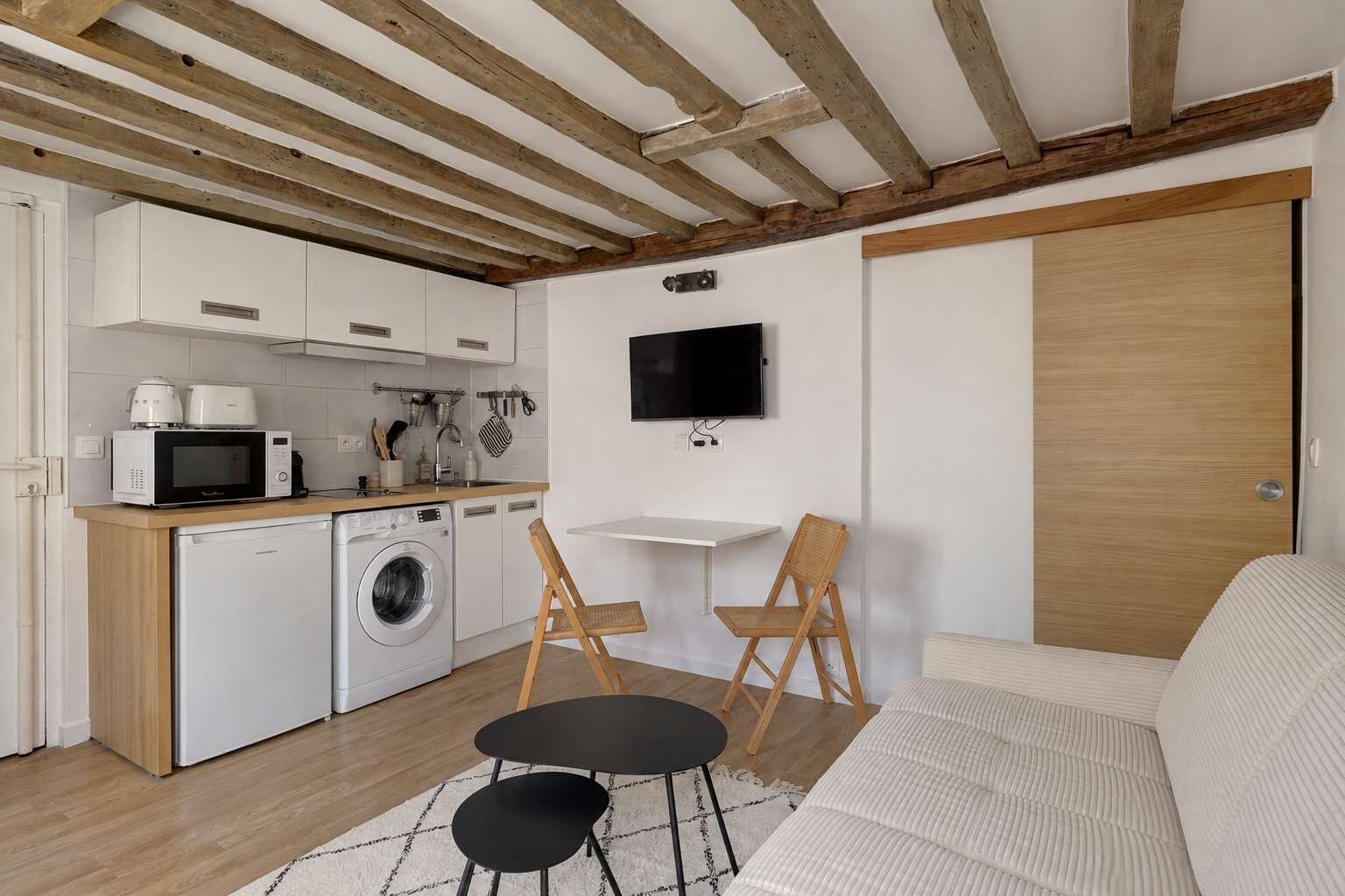 A compact living space with a kitchenette, a washing machine, a dining area with two chairs, and a sofa.