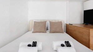 Una camera d'albergo con un letto, due cuscini, un comodino in legno, una televisione e degli asciugamani.