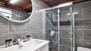 Un bagno moderno con doccia vetrata, lavandino bianco e specchio, e pareti rivestite di piastrelle grigie.