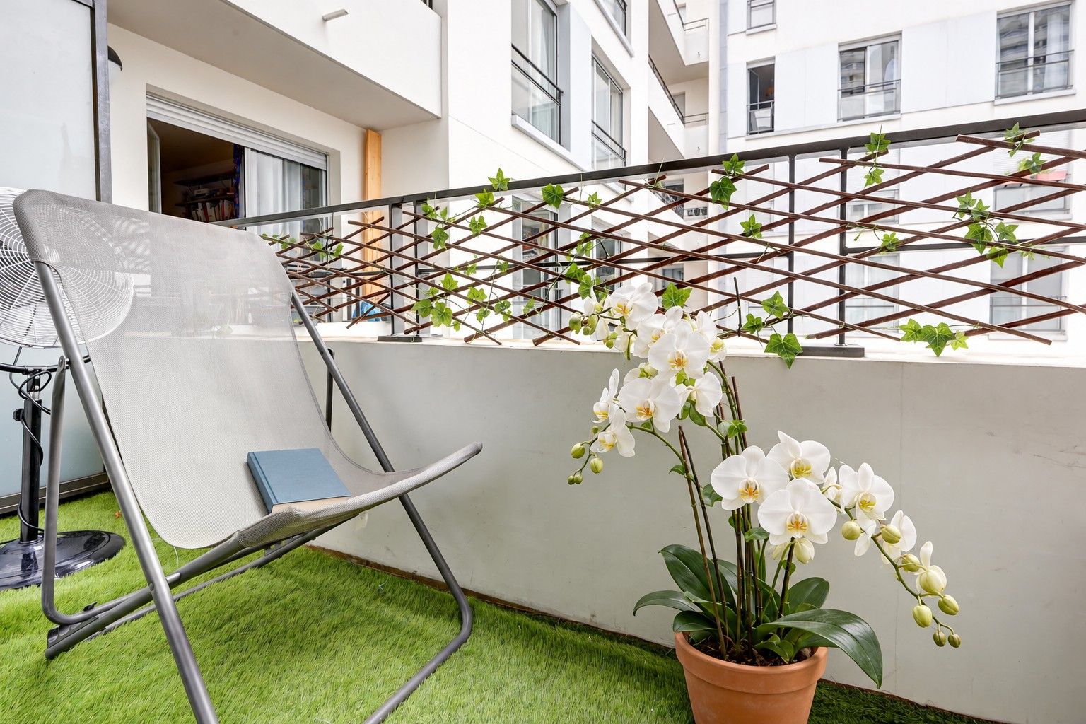 A balcony with a mesh chair, a potted orchid, and a trellis with climbing plants.