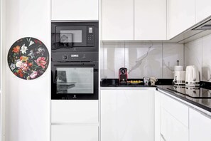 A kitchen with white cabinets, a black microwave, and a coffee maker. - Cocon lumineux avec balcon - Quartier Villette (Paris)