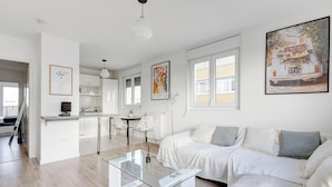 Ein modernes Wohnzimmer mit einem Glastisch, einem weißen Sofa mit grauen Kissen und einem Essbereich mit einem weißen Stuhl und Tisch.