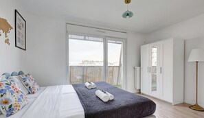 A modern bedroom with a large bed, a balcony with a view, and a wardrobe. - Cozy & Spacious Apartment 2BR/5P – Malakoff (Malakoff)