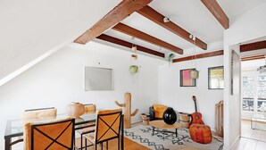 Un loft acogedor con vigas de madera a la vista, una zona de comedor con mesa de vidrio y vistas a la ciudad a través de amplios ventanales.