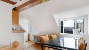 Un loft moderno con comedor que incluye una mesa de vidrio y sillas de madera, cocina con electrodomésticos integrados y un amplio ventanal con vista a la ciudad.