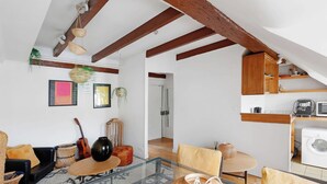 Amplia sala de estar con una mesa de centro de vidrio, un sofá y una mesa de comedor. Se observa una cocina con armarios de madera y una lavadora.