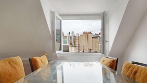 Un comedor moderno con una mesa de vidrio y sillas amarillas, con vistas a un paisaje urbano que incluye edificios y cielo despejado.