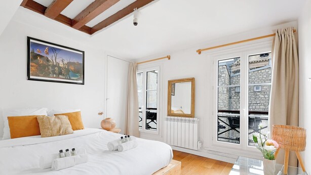 Habitación de hotel con una cama grande, un cuadro, un espejo y vistas a la ciudad a través de una ventana.
