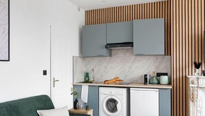 A compact kitchen with grey cabinets, a built-in washing machine, and a wooden slatted wall design. - Studio d'Architecte avec Cheminee - Design -4 personnes (Paris)