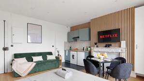 A modern living space with a green sofa, a dining table with chairs, a kitchen area, and a TV displaying 'NETFLIX'. - Studio d'Architecte avec Cheminee - Design -4 personnes (Paris)