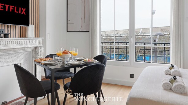 A modern hotel room with a dining area, a large window with a view, a fireplace, and a bed with rolled towels. - Studio d'Architecte avec Cheminee - Design -4 personnes (Paris)