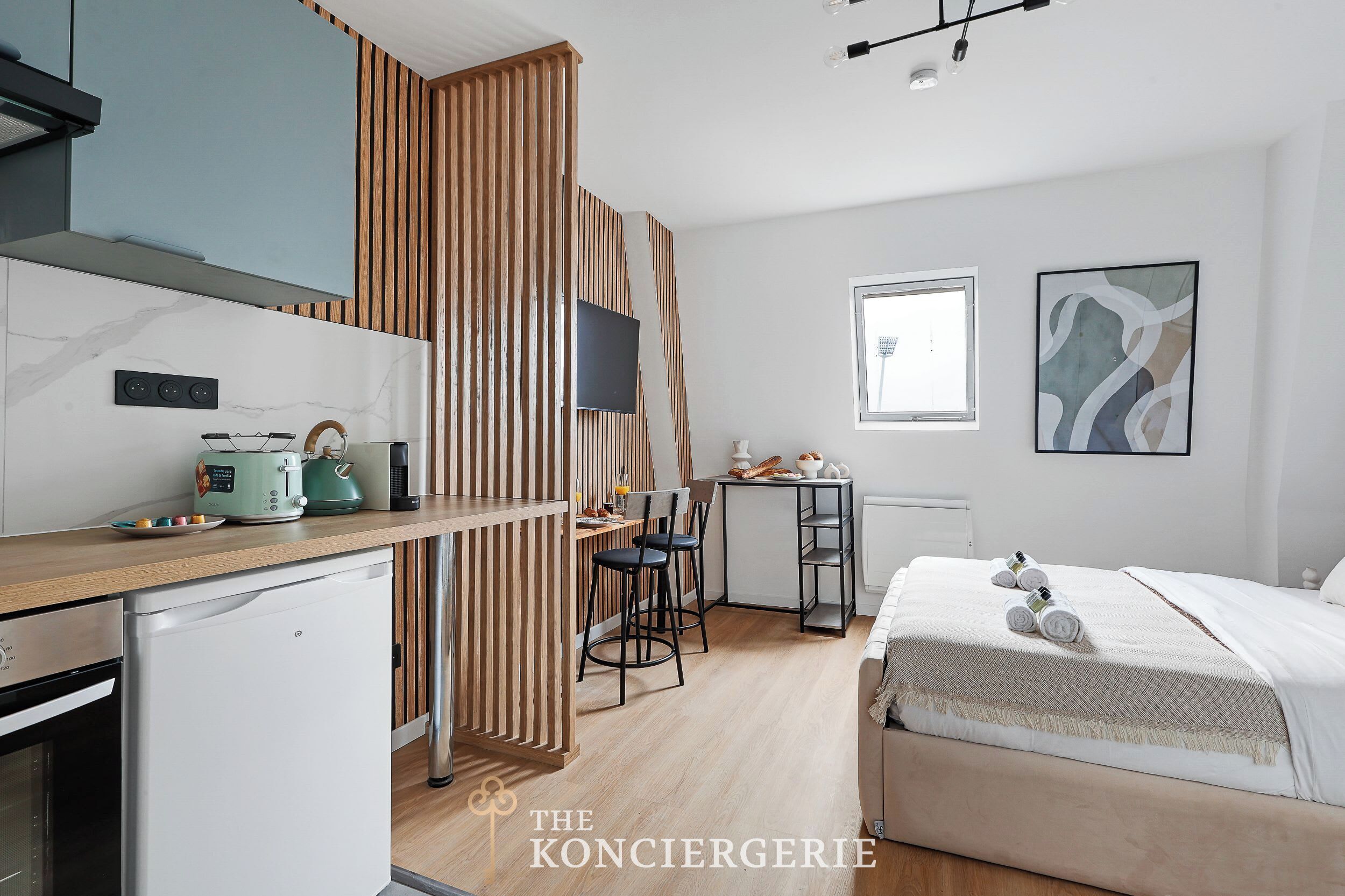Ein kleines Hotelzimmer mit Küchenzeile, Essbereich und Bett.