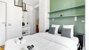 Hotellihuone, jossa on suuri sänky, vaatekaappi, peili ja yksi seinä on maalattu vihreällä värillä, mikä tuo huoneeseen väriä.