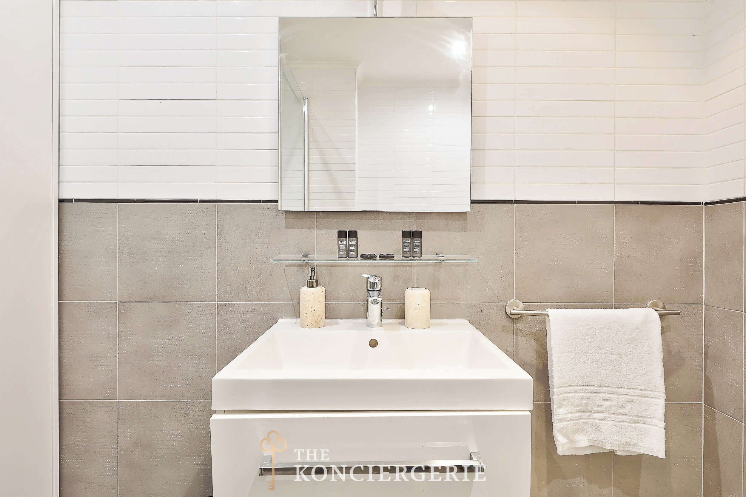 Une salle de bain avec un lavabo blanc, un miroir au-dessus et un porte-serviettes sur la droite.