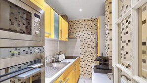 A compact kitchen with modern appliances, a sink, and yellow cabinets. - BM Magnifique Studio avec terrasse - Arc de Triomphe (Paris)