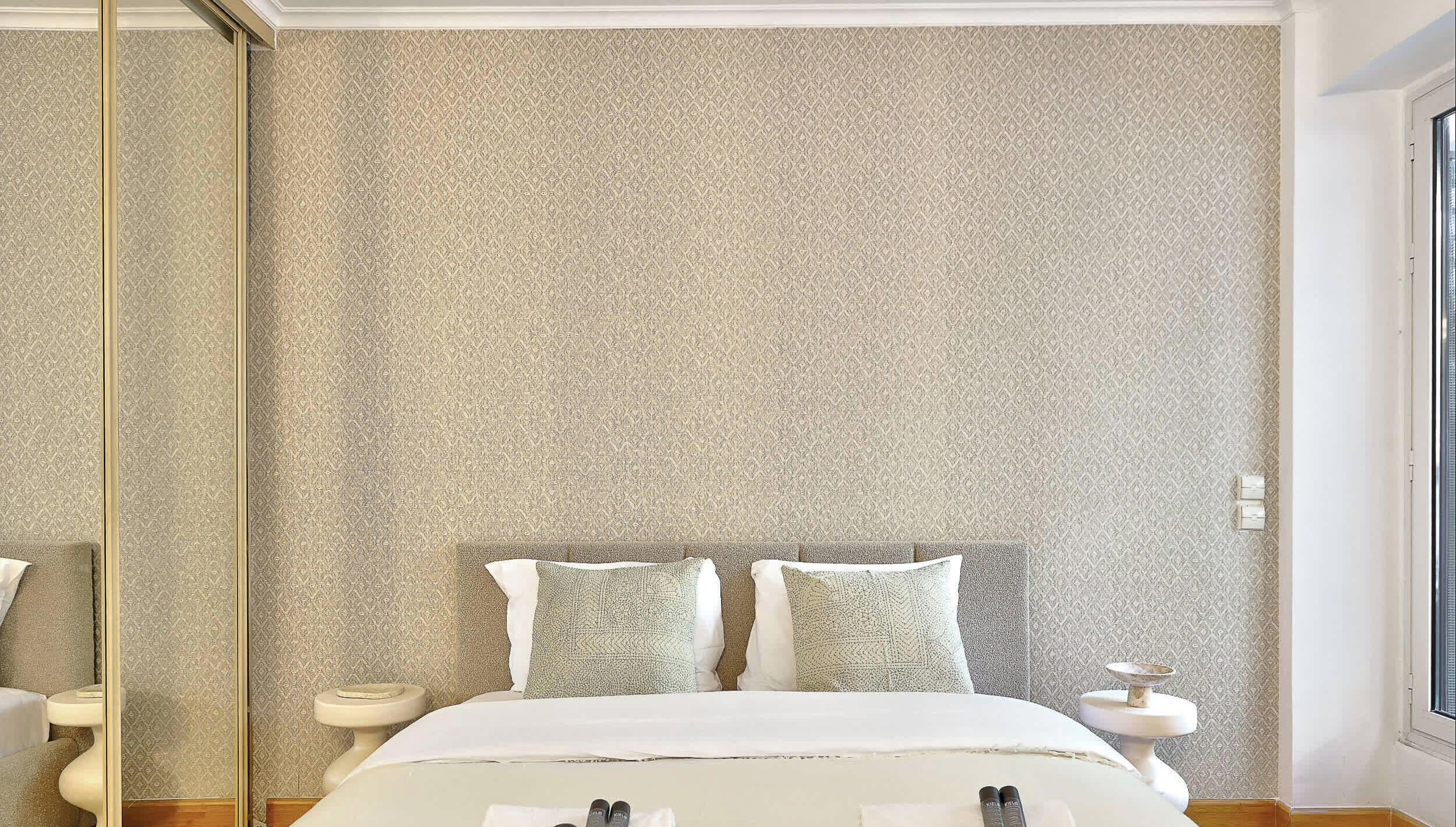 Un dormitorio con un espejo grande, una cama con ropa de cama blanca y papel tapiz estampado.