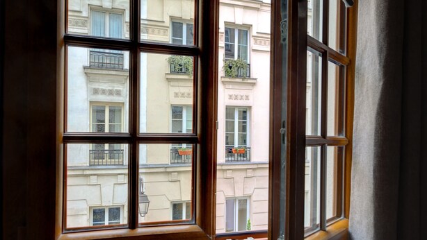 A window with multiple panes, revealing a building with balconies and windows. - Sunny Haven in Historic Le Marais (Paris)