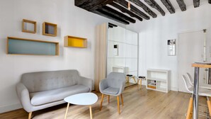 A modern living room with a grey sofa, a small round table, a grey armchair, and wooden flooring. - Sunny Haven in Historic Le Marais (Paris)