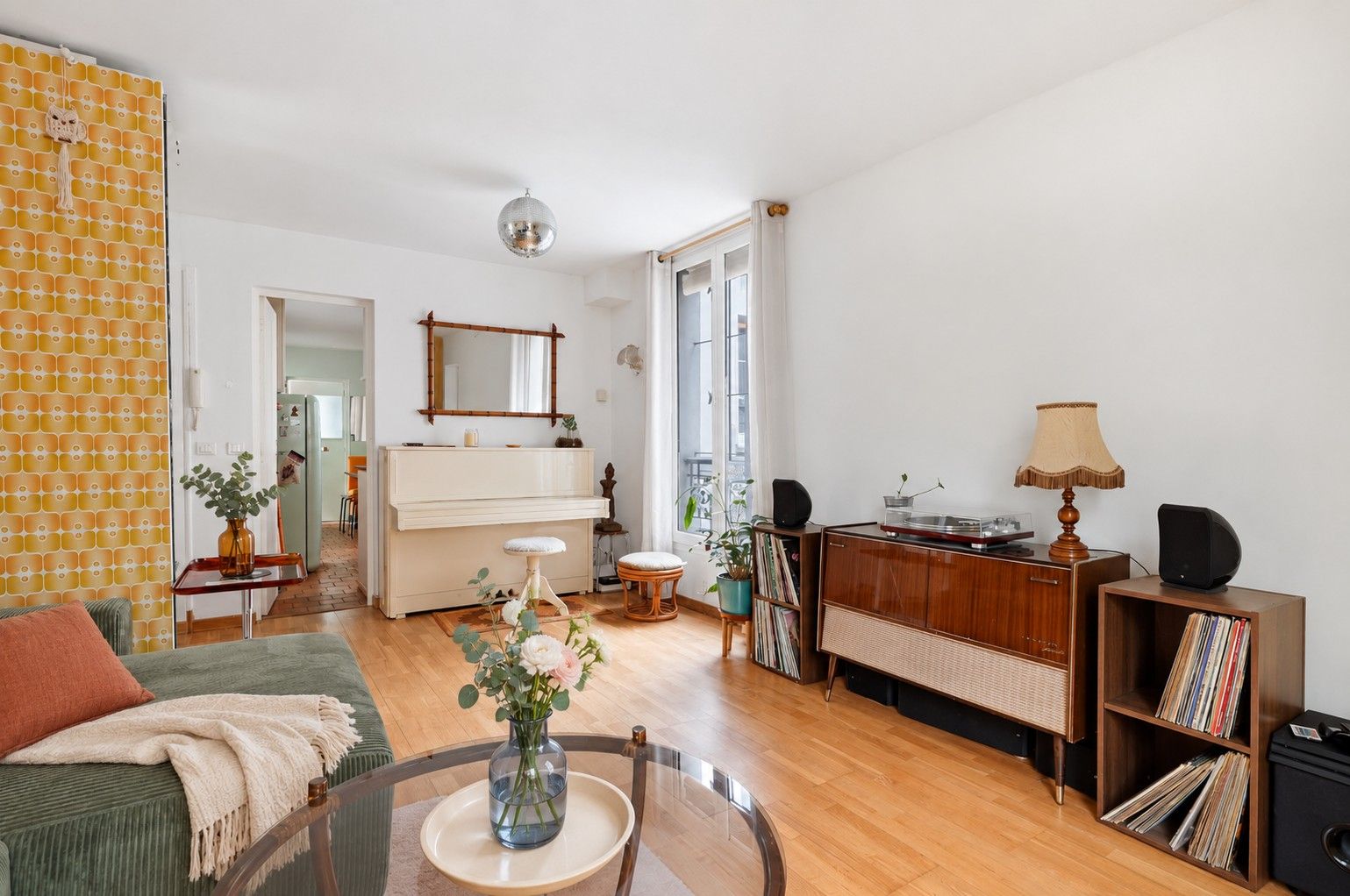 A living room with a piano, a glass coffee table with a vase, a sofa, and a bookshelf.