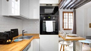 A modern kitchen with white cabinets, a wooden countertop, a built-in oven, and a dining area with a table and chairs. - Sunny Haven in Historic Le Marais (Paris)