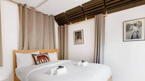 A hotel room with a bed, curtains, a wooden headboard, a pillow, a framed picture, and a rolled towel. - Sunny Haven in Historic Le Marais (Paris)