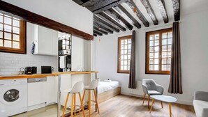 A compact kitchen with a washing machine, a dining area with stools, and a bed with a window. - Sunny Haven in Historic Le Marais (Paris)