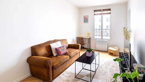 Una sala de estar con un sofá de cuero marrón, una mesa de centro negra y una mesita auxiliar con una planta.