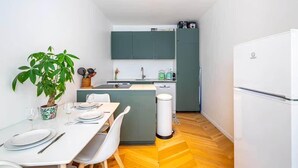 Cocina compacta con comedor, una planta en maceta y un cubo de basura blanco.