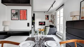 Un salon moderne avec un coin repas, comprenant un téléviseur à écran plat, des œuvres d’art et une grande fenêtre.