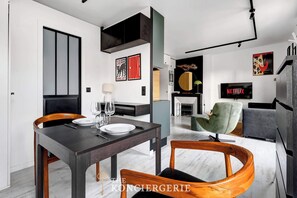 Ein modernes Wohnzimmer mit Essbereich, ausgestattet mit einem dunklen Holztisch, Holzstühlen, einem grünen Sessel und einem grauen Sofa.
