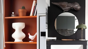 Une pièce avec une bibliothèque remplie de livres, un cactus en pot, un vase blanc et une figurine de poulet blanc. Un miroir noir est accroché au mur et une lampe verte se trouve sur une table noire.
