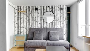 Ein modernes Wohnzimmer mit einem grauen Sofa, einem runden Spiegel und einer hellblauen Kommode.