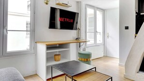 Ein modernes Wohnzimmer mit einem an der Wand montierten Flachbildfernseher, einem hölzernen Konsolentisch, einem kleinen runden Hocker und einem Korbwäschekorb.
