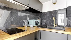 Eine moderne Küche mit schwarzem Marmor als Rückwand, einer hellblauen Mikrowelle, einem goldenen Wasserhahn und einem eingebauten Backofen.
