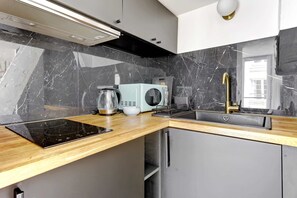A modern kitchen with a black marble backsplash, a light blue microwave, a gold faucet, and a built-in oven. - Studio lumineux au centre de Paris (Paris)