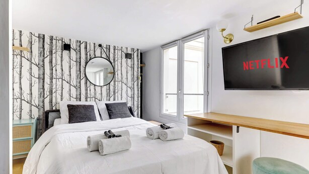 Ein modernes Hotelzimmer mit einem großen Bett, einem an der Wand montierten Fernseher, einem Fenster und einem Spiegel.