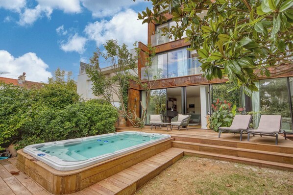 A modern house with a hot tub, outdoor seating, and a glass-enclosed patio.