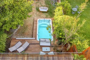An aerial view of a backyard with a hot tub, two lounge chairs, a small table, and a garden area.