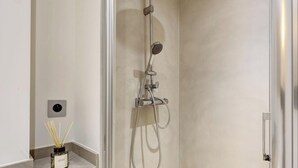 A modern bathroom with a shower, a wall-mounted light, and a reed diffuser on the floor. - Duplex d'Exception avec climatisation - Rue Monge (Paris)