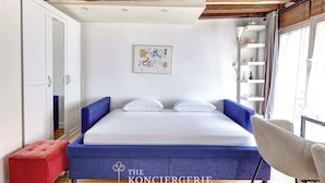 Una camera da letto con un letto, un poggiapiedi rosso, una sedia blu e un armadio bianco.