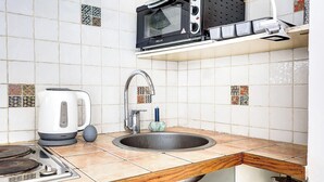 Una cucina con piastrelle bianche, un lavello, un bollitore, un fornello, un microonde e un rubinetto.